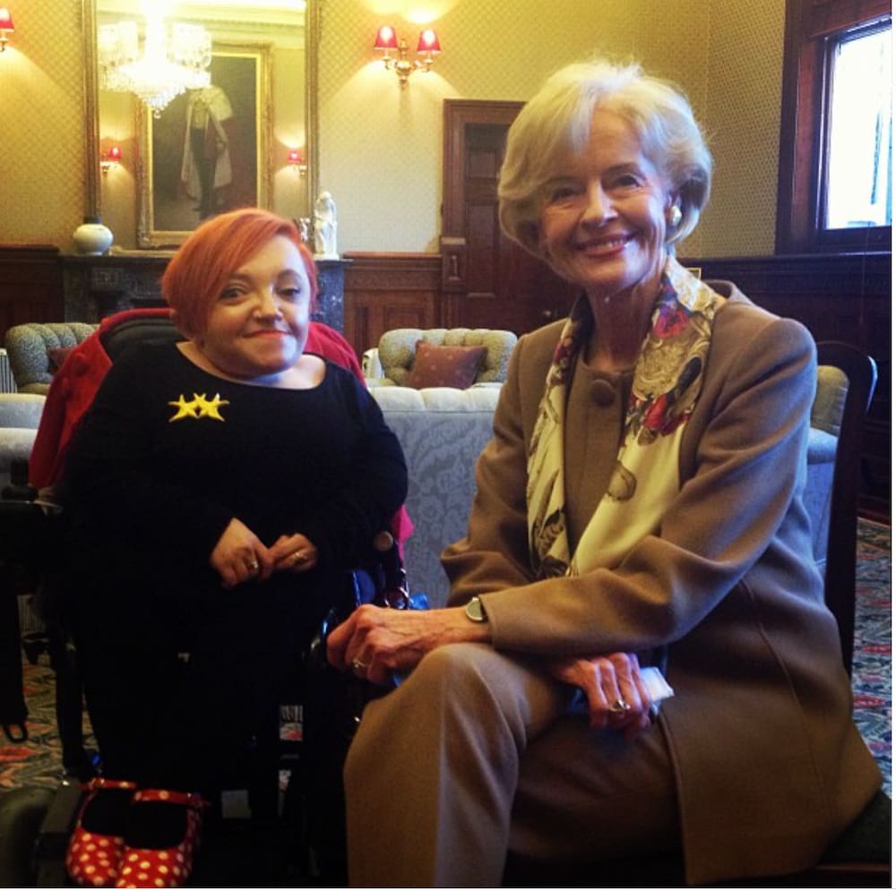 Stella and Govenor General Quentin Bryce sit together smiling in an elegant room. Stella's red spotted shoes are just visible and a star brooch is pinned to her top.