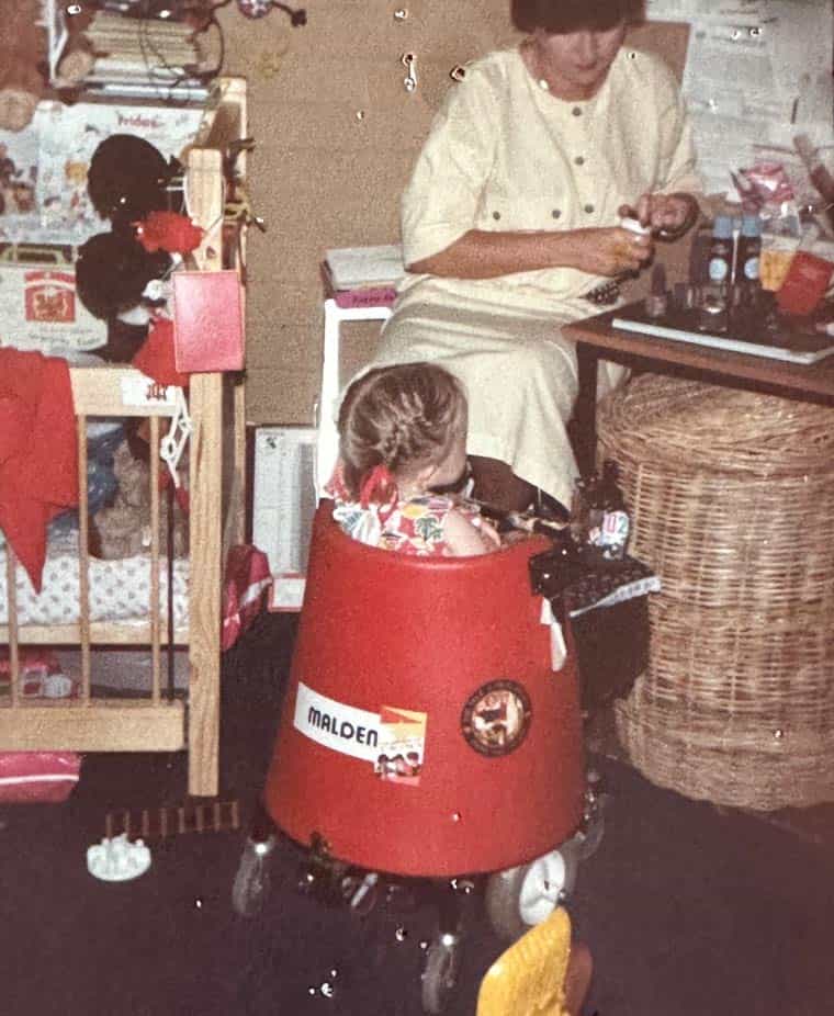Stella is in what looks to be a purpose built red mobility device. Mum Lynne sits at a table. They are in her hairdressing salon.